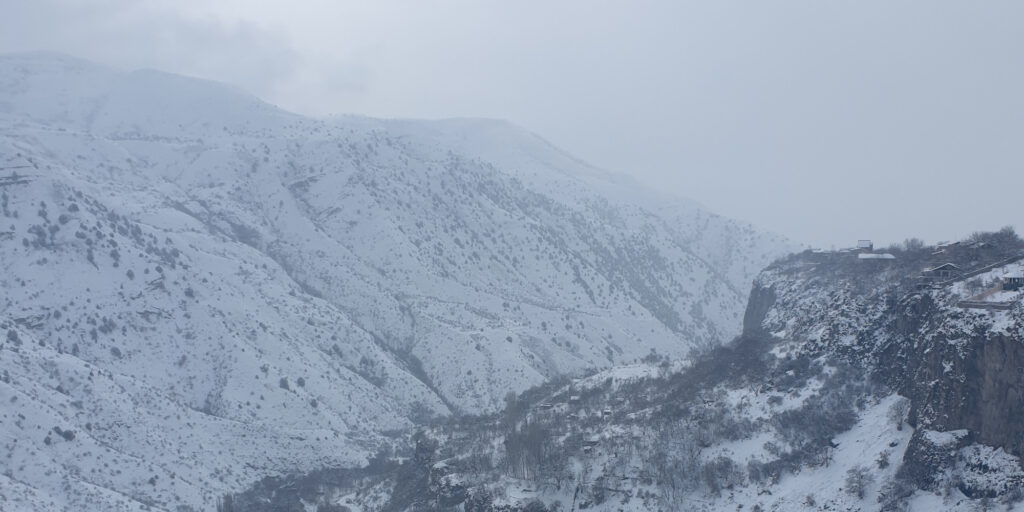 A mountainous landscape covered in snow, with snowy and foggy weather reducing visibility in the background.